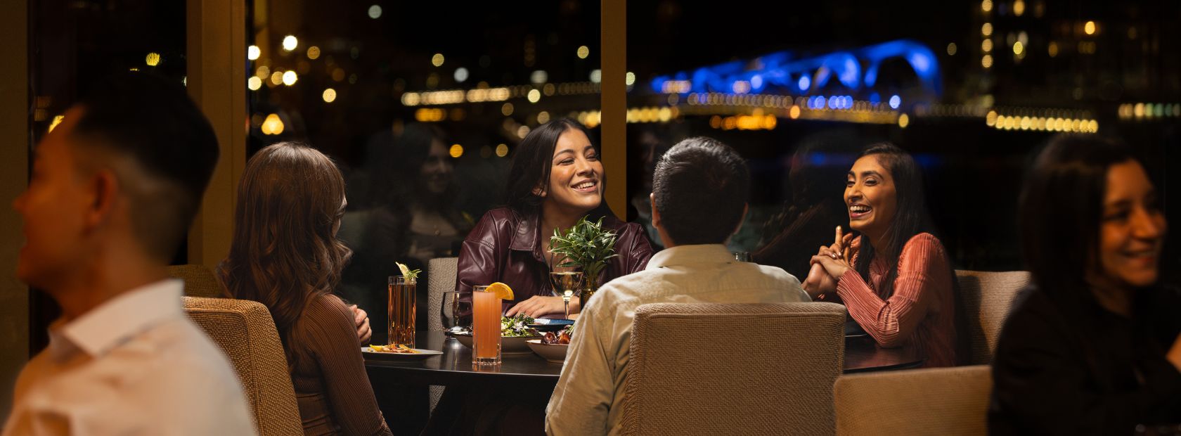 diners in Aura Waterfront Restaurant + Patio enjoying dinner with the city lit up in the background