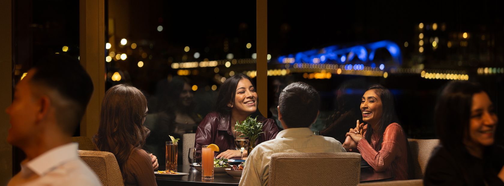 diners in Aura Waterfront Restaurant + Patio enjoying dinner with the city lit up in the background